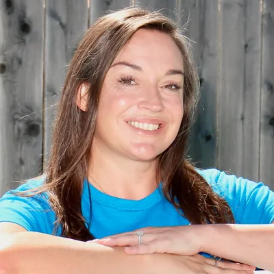 Jennifer Abraham smiling, arms folded on a rail in front of a wooden fence